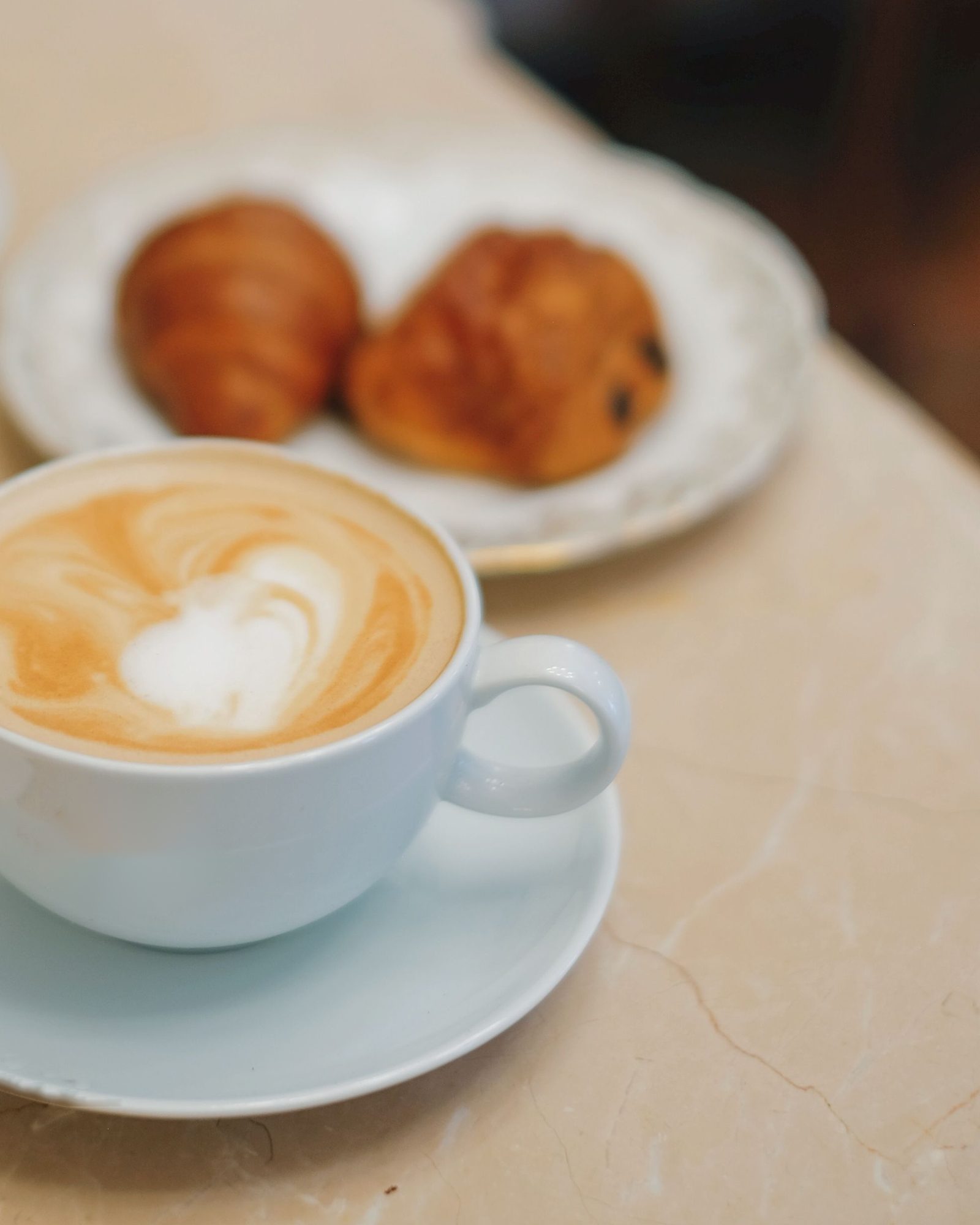 Cappuccino con latte art e due brioche sul tavolo in marmo