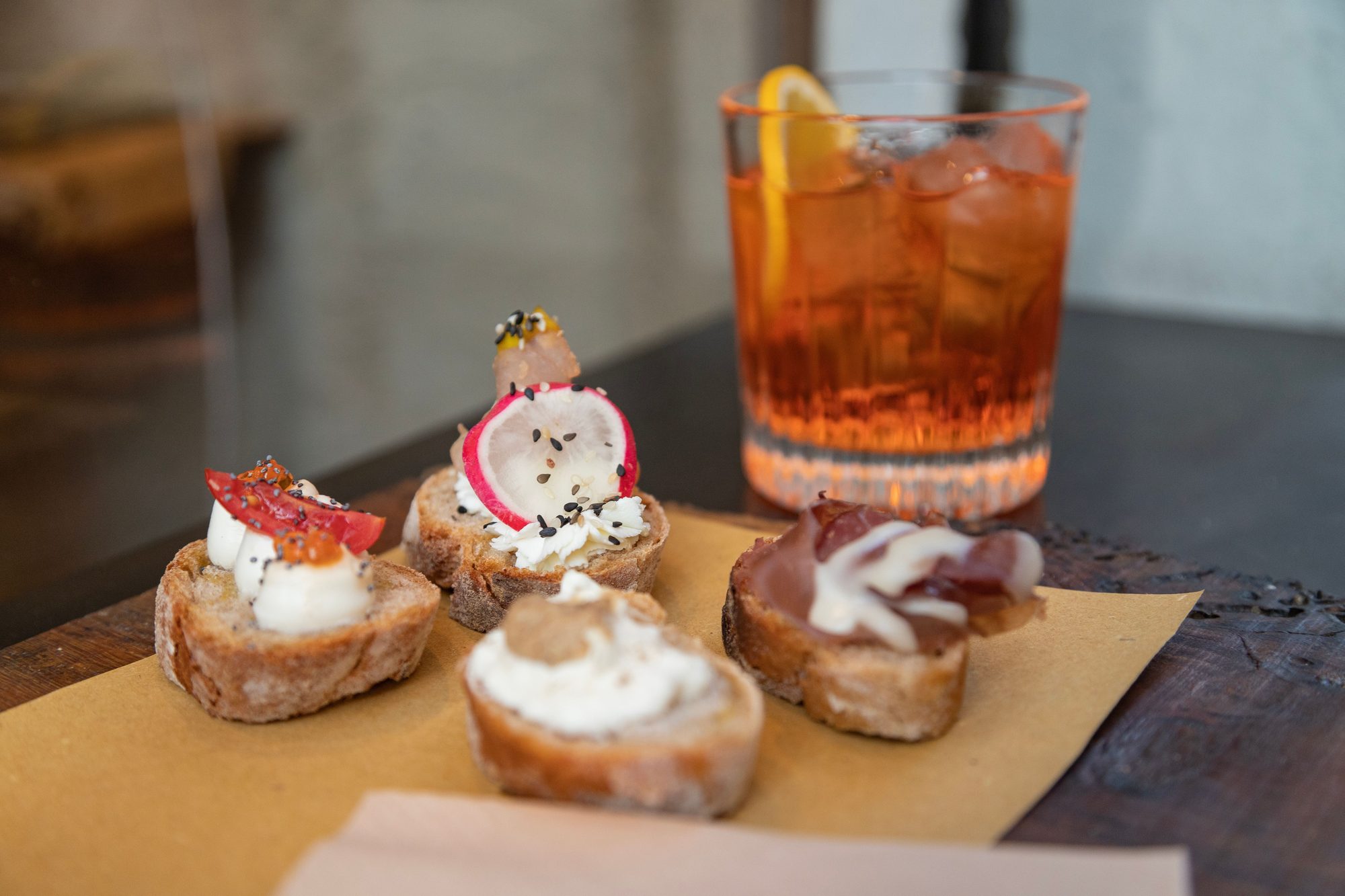 Spritz con ghiaccio e arancia accanto a quattro crostini su carta